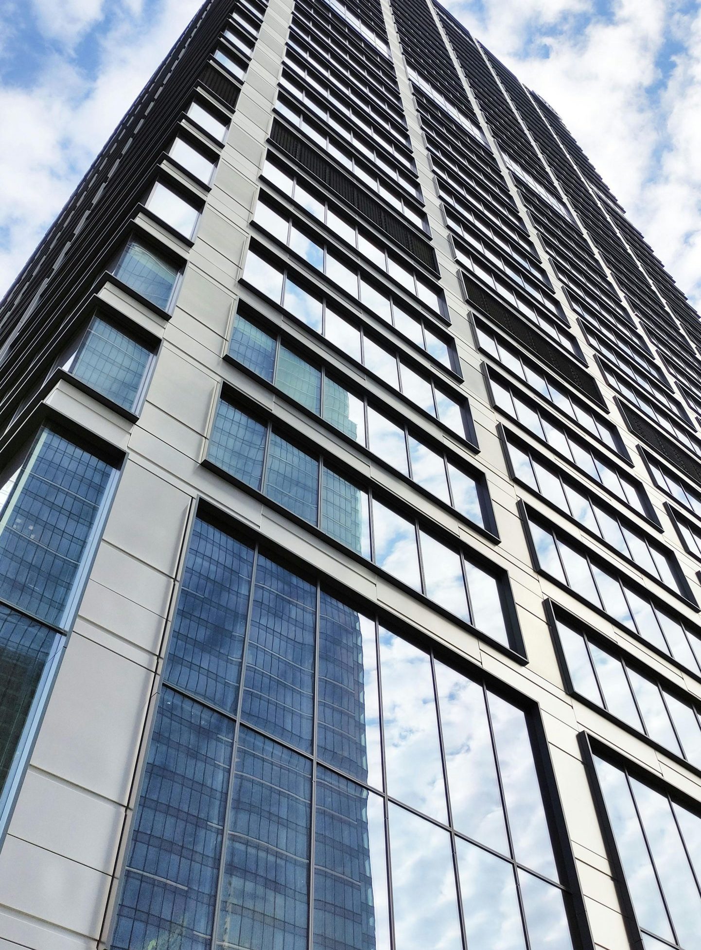 Home Vertical view of a modern skyscraper in Warsaw, captured from a striking low angle against a clear blue sky.