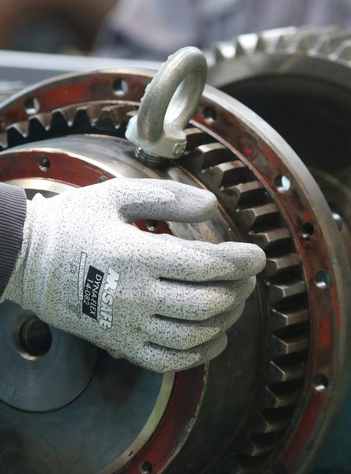 Home A gloved hand adjusts a gear in industrial machinery, focusing on precision.